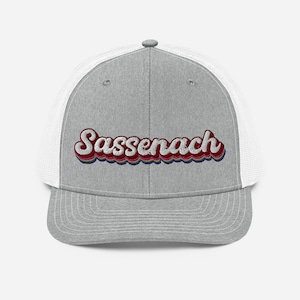 May include: A grey and white trucker hat with a retro-style embroidered design that says "Sassenach".