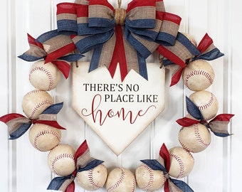 May include: A baseball-themed wreath with a red, white, and blue bow and a wooden home plate sign that reads "There's no place like home".