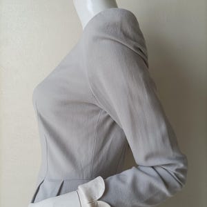 以下が含まれることがあります： 白い襟とカフスが付いたグレーのロングスリーブドレス。ドレスはフィットしたボディスとフルスカートです。