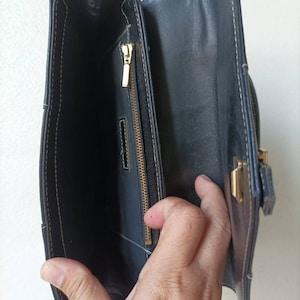 May include: A black leather purse with a gold zipper and clasp. The purse is open and the inside is visible.