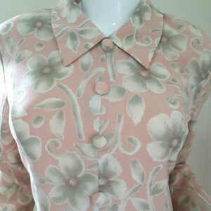 May include: A pink long-sleeved blouse with a floral print in shades of white and green. The blouse has a collared neckline and button closure.