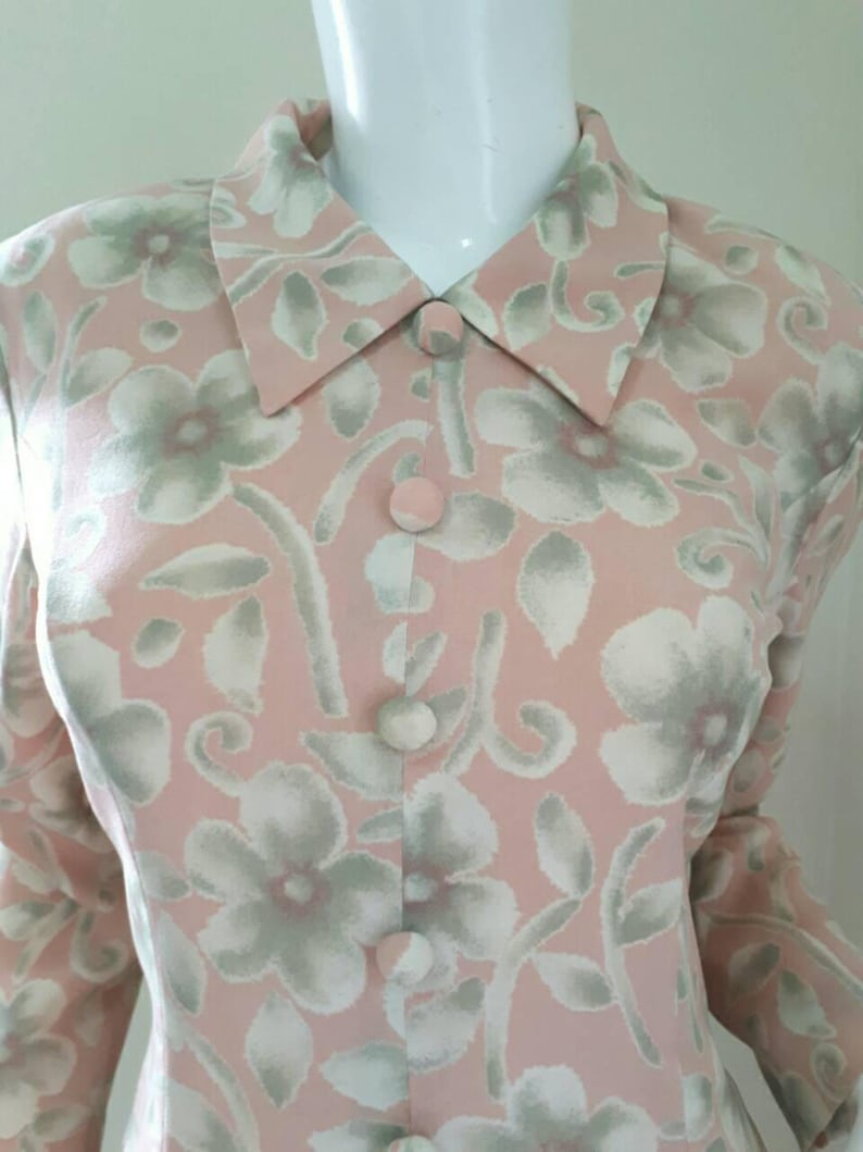 May include: A pink long-sleeved blouse with a floral print in shades of white and green. The blouse has a collared neckline and button closure.