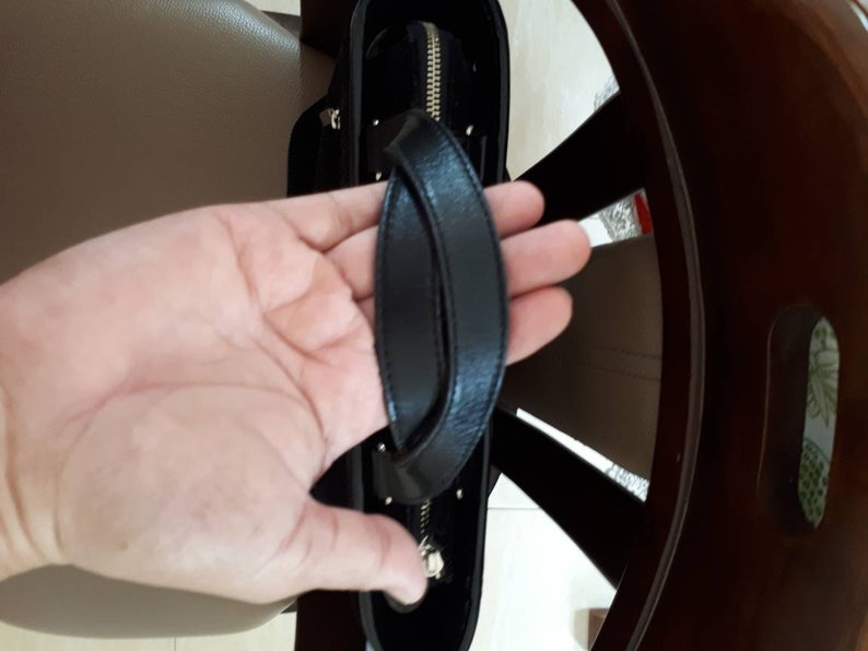 K&ouml;nnte beinhalten: Eine schwarze Ledertasche mit einem oberen Henkel und einem Rei&szlig;verschluss.