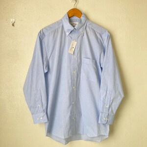 May include: A light blue long-sleeved button-down shirt with a white and light blue checkered pattern. The shirt has a pocket on the left side and a white tag with the text "Country Club Prep" on the front.