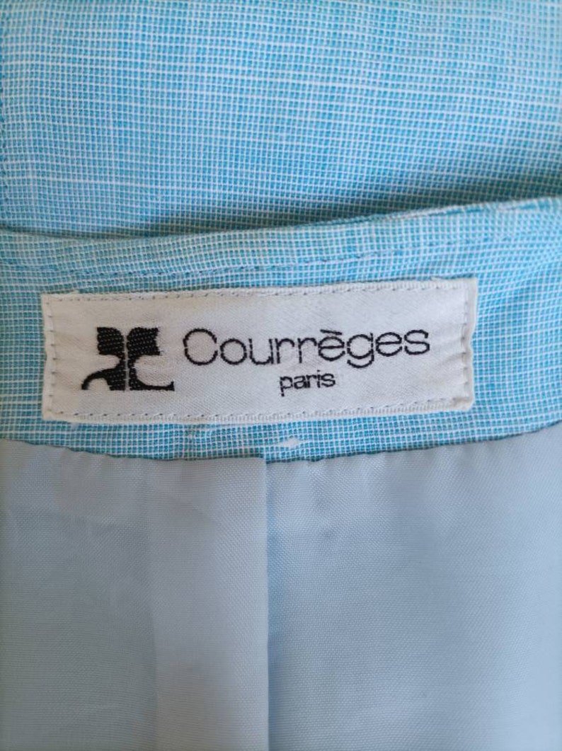May include: A white label with black text that reads "Courr&egrave;ges Paris" on a light blue fabric background.