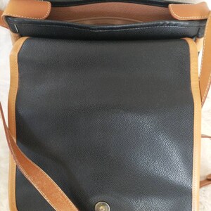 May include: A black leather shoulder bag with a brown leather trim and strap. The bag has a flap closure and a single buckle.