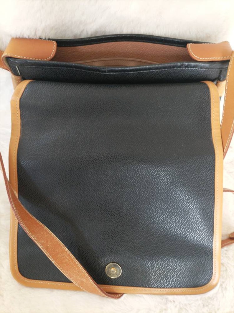 May include: A black leather shoulder bag with a brown leather trim and strap. The bag has a flap closure and a single buckle.