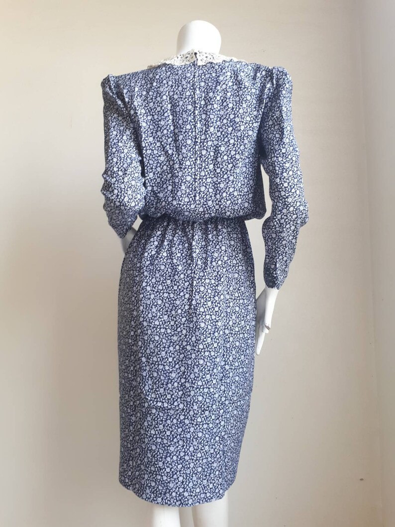 May include: A blue and white floral print dress with a white lace collar. The dress has long sleeves and a fitted silhouette.