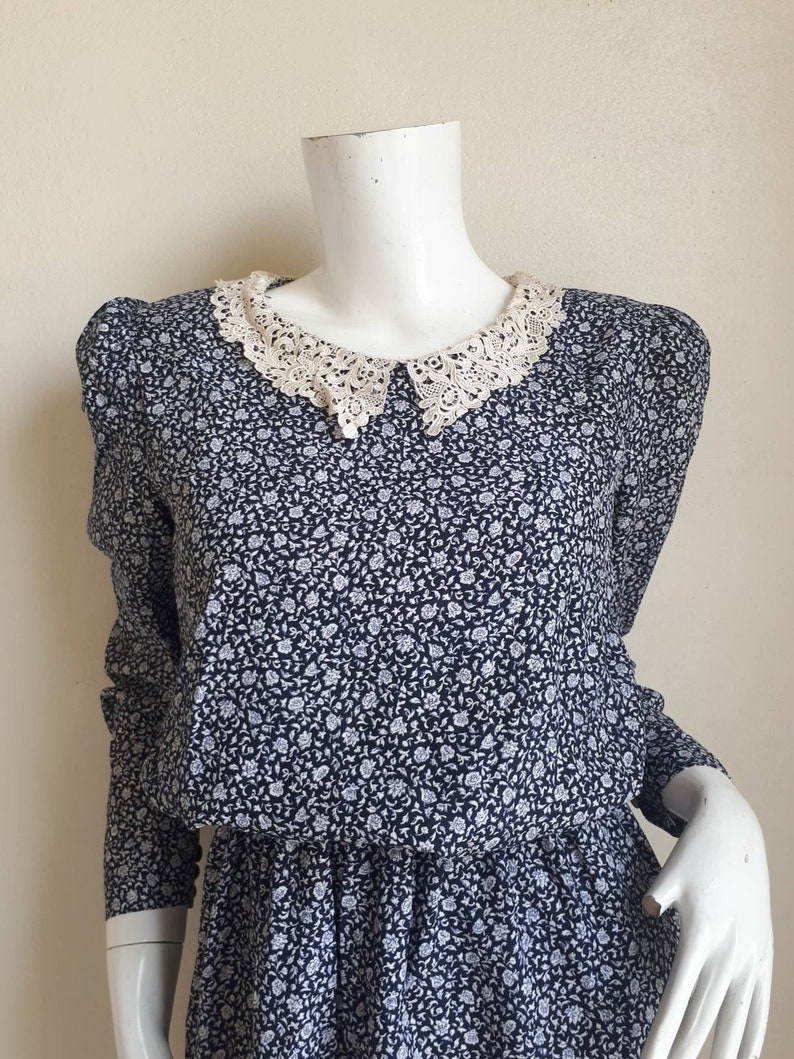 May include: A vintage floral dress with a white lace collar. The dress has a fitted bodice and a gathered skirt. The fabric is a lightweight cotton blend.