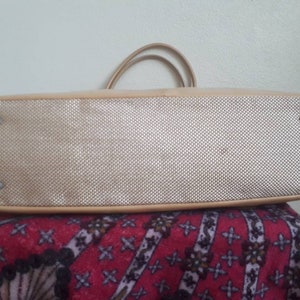 May include: The underside of a beige tote bag with a woven fabric lining. The bag has two handles and four silver studs.