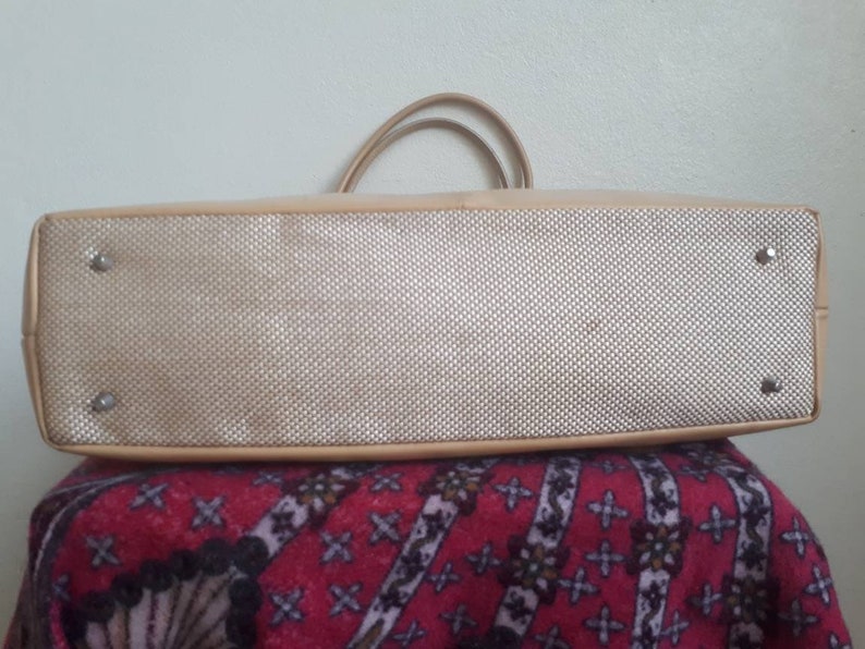 May include: The underside of a beige tote bag with a woven fabric lining. The bag has two handles and four silver studs.