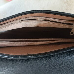 May include: The inside of a black leather handbag with a brown leather trim. The bag has two zippered compartments.