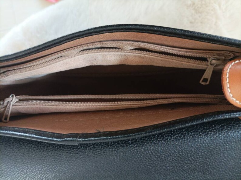 May include: The inside of a black leather handbag with a brown leather trim. The bag has two zippered compartments.