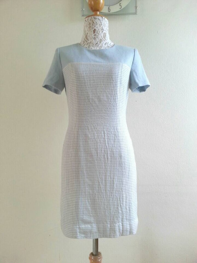 May include: A light blue dress with a white and light blue checkered pattern. The dress has short sleeves and a fitted silhouette.