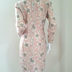 May include: A pink dress with a floral pattern. The dress has long sleeves and a fitted silhouette.