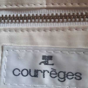 K&ouml;nnte beinhalten: Wei&szlig;e Ledertasche mit einem silbernen Rei&szlig;verschluss und einem wei&szlig;en Etikett mit dem Text "Courr&egrave;ges" in schwarzen Buchstaben.