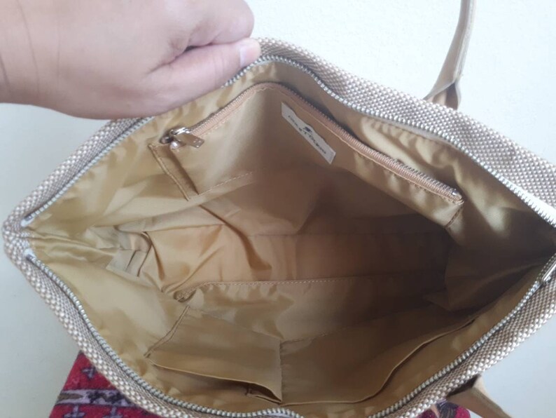 May include: Beige canvas tote bag with a zip closure and a small zipped pocket inside. The bag has a beige fabric lining.