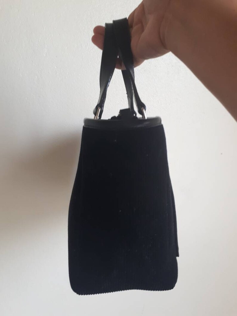 K&ouml;nnte beinhalten: Eine schwarze Samt-Handtasche mit einem Henkel oben und silbernen Beschl&auml;gen.