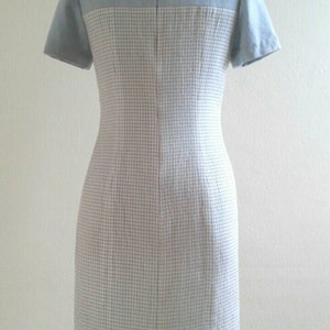 May include: A light blue and white checkered dress with short sleeves. The dress has a fitted silhouette and a back zipper closure.