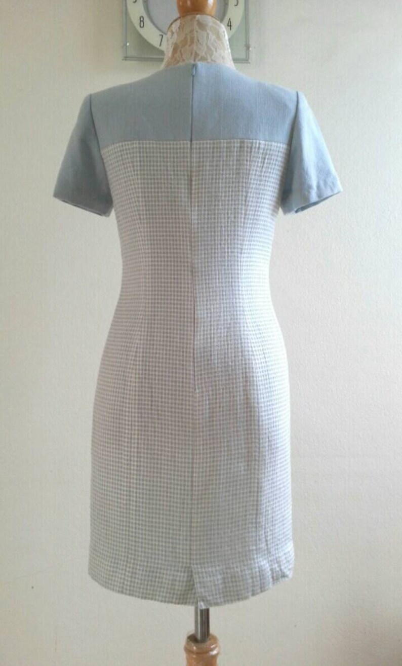 May include: A light blue and white checkered dress with short sleeves. The dress has a fitted silhouette and a back zipper closure.