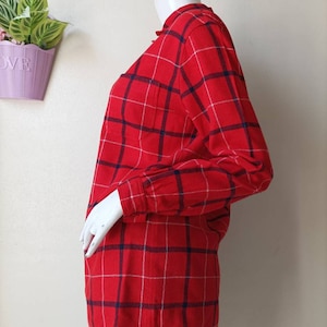 May include: Red and white plaid long-sleeve shirt with a blue trim. The shirt has a button-up front and a pocket on the left chest.