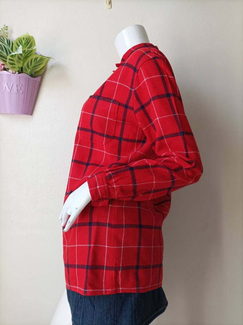 May include: Red and white plaid long-sleeve shirt with a blue trim. The shirt has a button-up front and a pocket on the left chest.