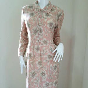 May include: A pink and green floral print dress with a collared neckline and long sleeves. The dress has a button-up front and a fitted silhouette.