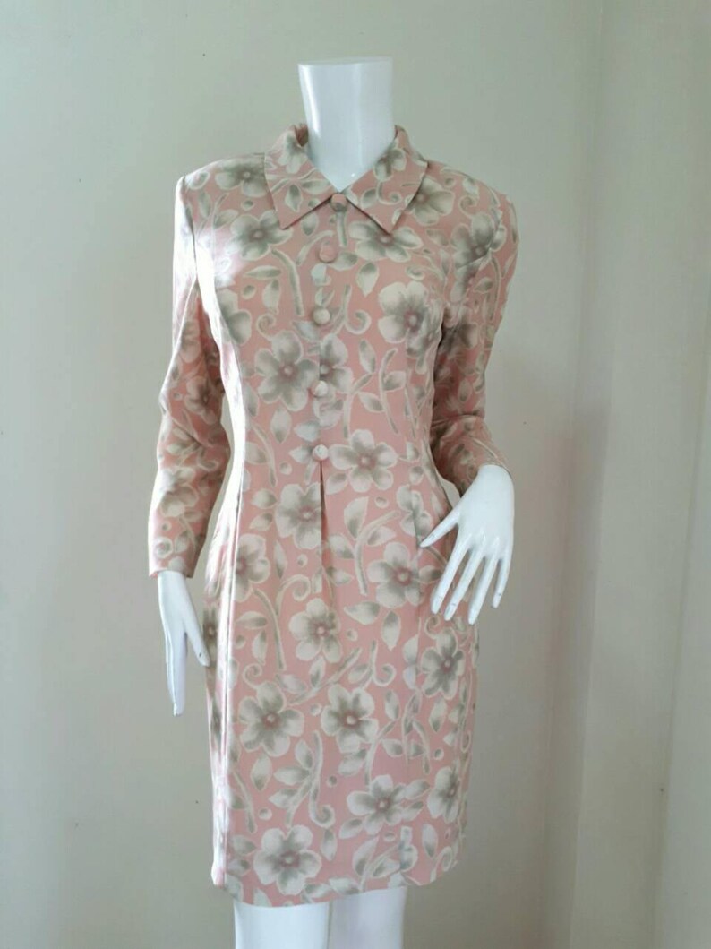 May include: A pink and green floral print dress with a collared neckline and long sleeves. The dress has a button-up front and a fitted silhouette.