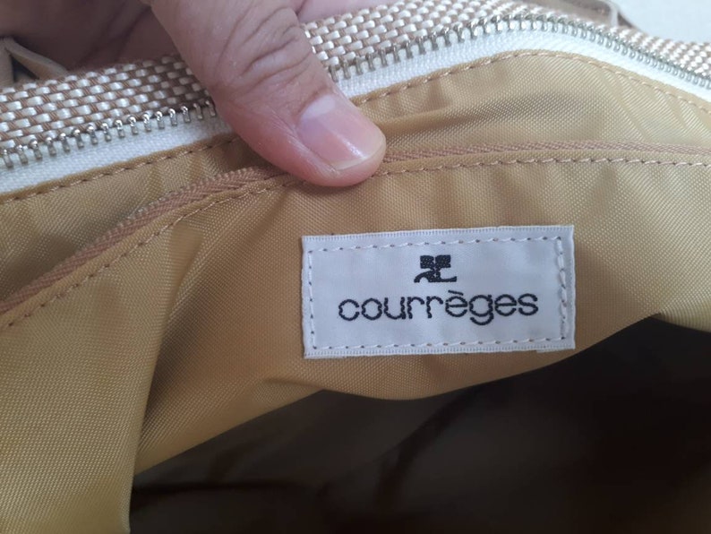 May include: A beige fabric bag with a white zipper and a white label that says "Courr&egrave;ges" in black text.