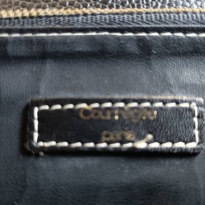 May include: Close-up of a black leather wallet with white stitching. The wallet has a small label that reads "Courr&egrave;ges Paris".