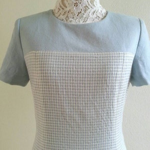 May include: A light blue dress with a white and light blue checkered pattern. The dress has short sleeves and a round neckline.