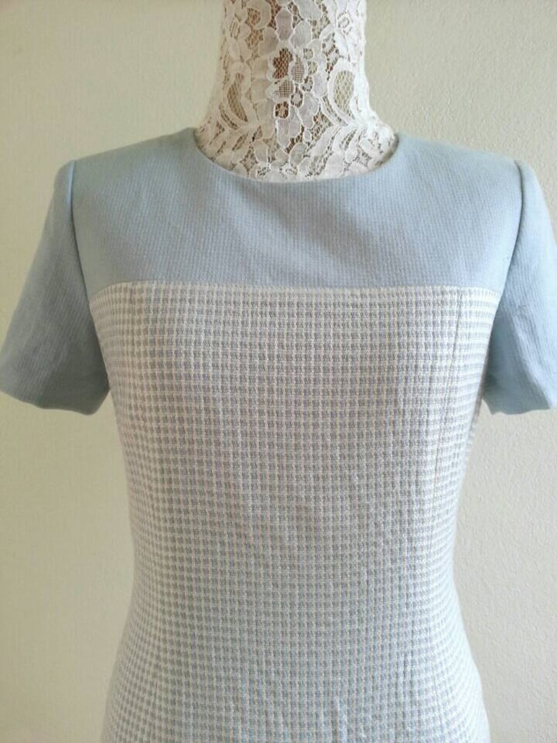 May include: A light blue dress with a white and light blue checkered pattern. The dress has short sleeves and a round neckline.