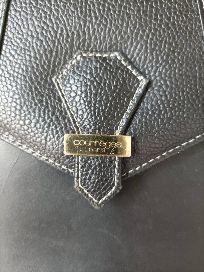 May include: Close-up of a black leather purse with a gold metal tag that reads "Courr&egrave;ges Paris".
