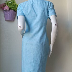 May include: A light blue short-sleeved dress with a collared neckline. The dress is made of a linen fabric and has a straight silhouette.