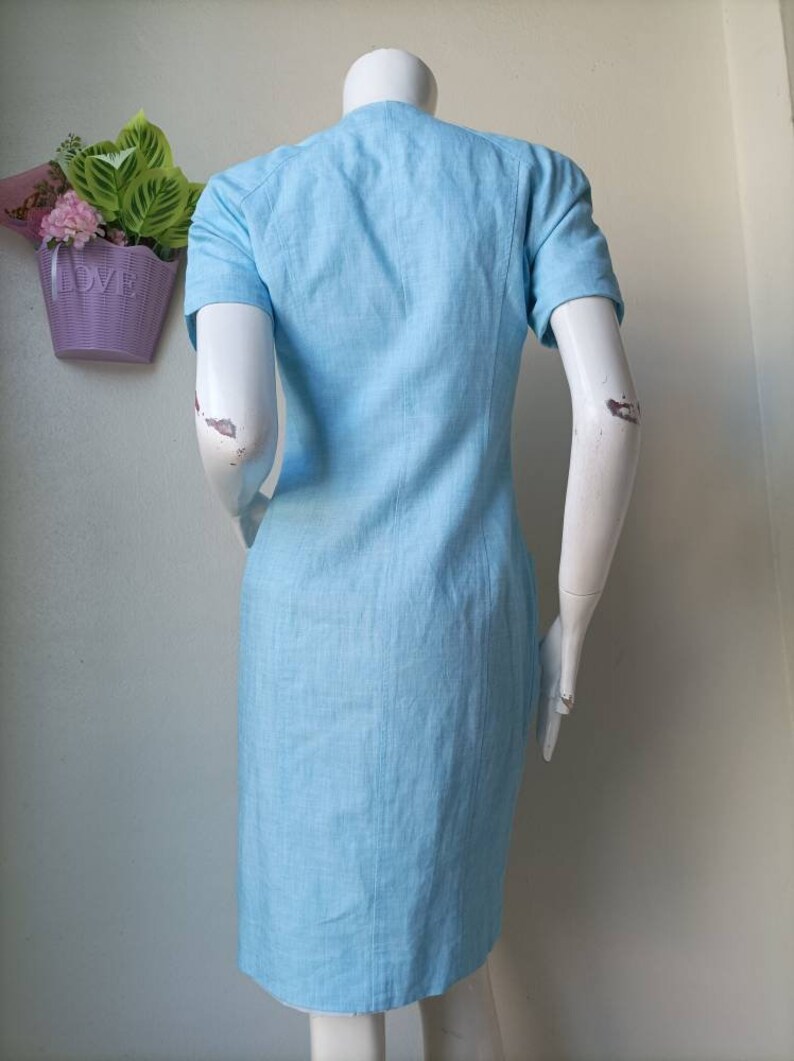May include: A light blue short-sleeved dress with a collared neckline. The dress is made of a linen fabric and has a straight silhouette.