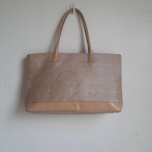 May include: A beige tote bag with a woven texture and a brown leather trim. The bag has two top handles.