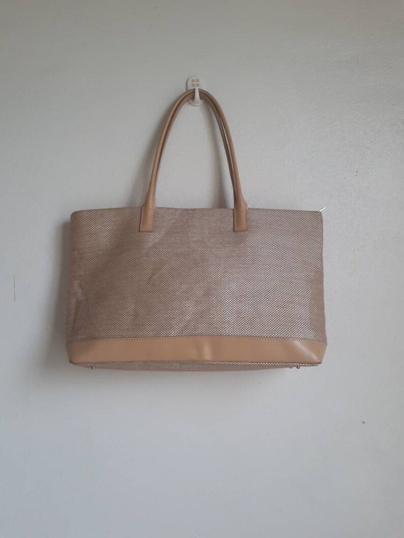 May include: A beige tote bag with a woven texture and a brown leather trim. The bag has two top handles.