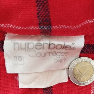 May include: A white label with the text "hyperbole" Courr&egrave;ges&reg; Paris on a red and white plaid fabric background.