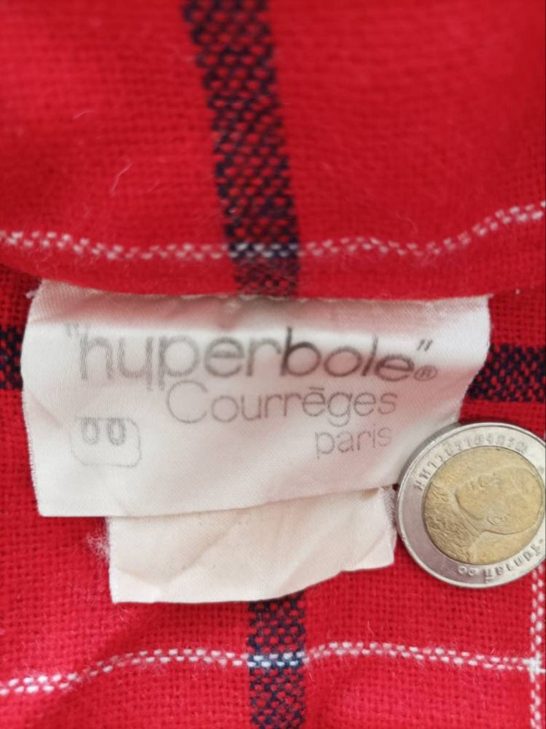 May include: A white label with the text "hyperbole" Courr&egrave;ges&reg; Paris on a red and white plaid fabric background.