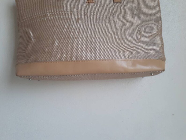 May include: A beige tote bag with a woven texture and a brown leather trim.