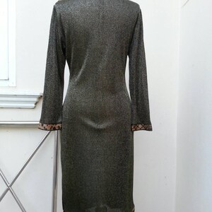 May include: A long-sleeved, gold metallic dress with a brown and black patterned trim around the collar and hem. The dress has a mandarin collar and a fitted silhouette.