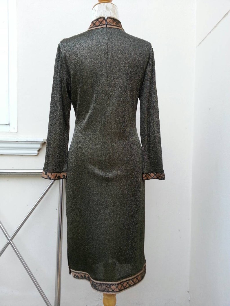 May include: A long-sleeved, gold metallic dress with a brown and black patterned trim around the collar and hem. The dress has a mandarin collar and a fitted silhouette.