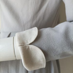 以下が含まれることがあります： 白い襟とカフスが付いたグレーのドレス。カフスは波状の縁取りがされています。