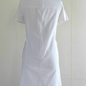 May include: A white short-sleeved dress with a simple design. The dress has a round neckline and a zipper in the back.