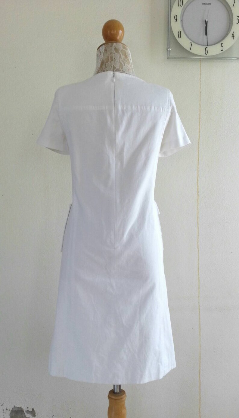 May include: A white short-sleeved dress with a simple design. The dress has a round neckline and a zipper in the back.