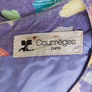 May include: A white label with the text "Courr&egrave;ges Paris" in black lettering. The label is attached to a purple fabric with a colorful geometric pattern.