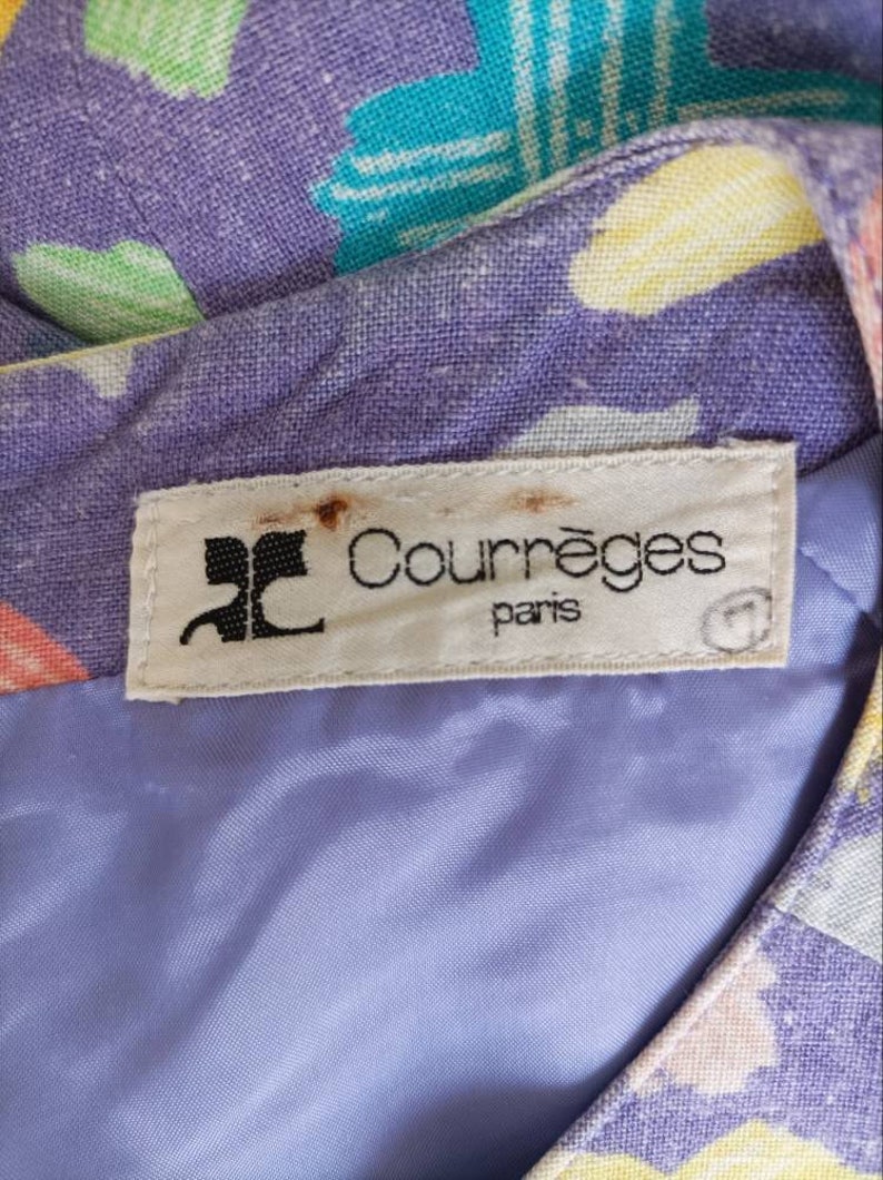 May include: A white label with the text "Courr&egrave;ges Paris" in black lettering. The label is attached to a purple fabric with a colorful geometric pattern.