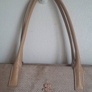 May include: A beige woven tote bag with leather handles and a small metal logo on the front.
