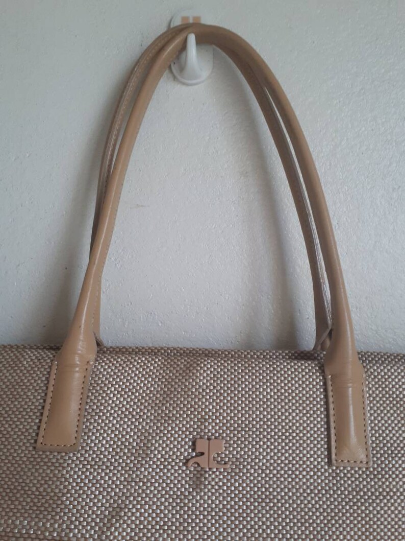 May include: A beige woven tote bag with leather handles and a small metal logo on the front.