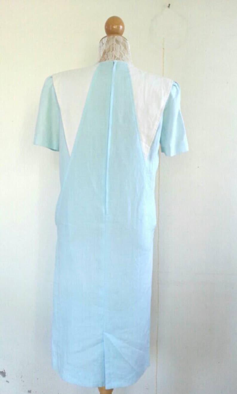 May include: A light blue dress with a white collar and short sleeves. The dress is on a mannequin.